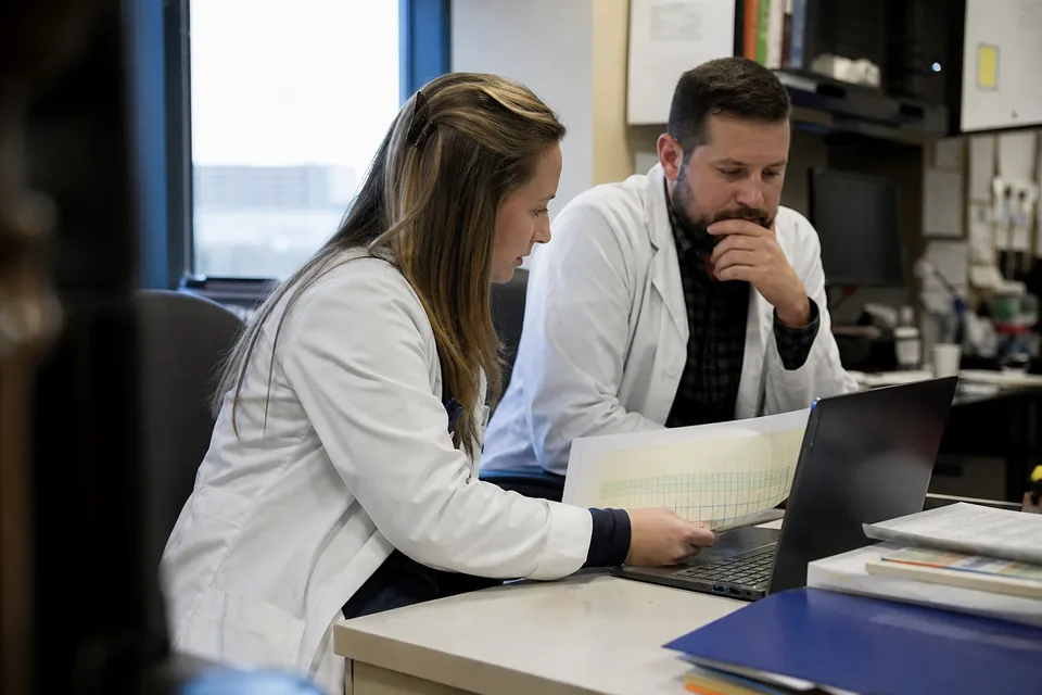 Clinical pharmacist and laboratory manager reviewing a printed antibiogram and a laptop in a health system office